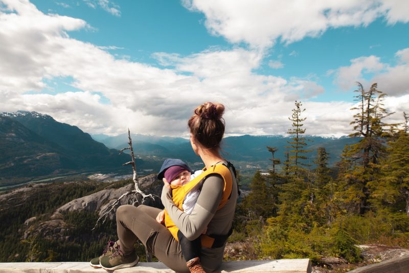 Middle-aged mother holding nursing baby to her chest while looking out at mountain view.