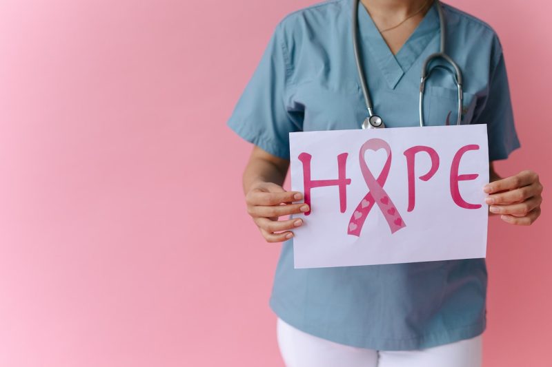 Female doctor holding sign that says hope with breast cancer symbol.