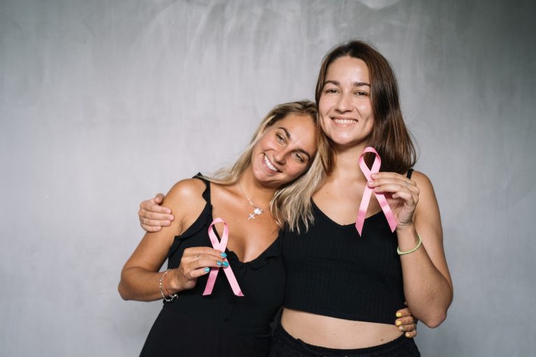 Two women holding pink ribbons to honor breast cancer awareness month in October.