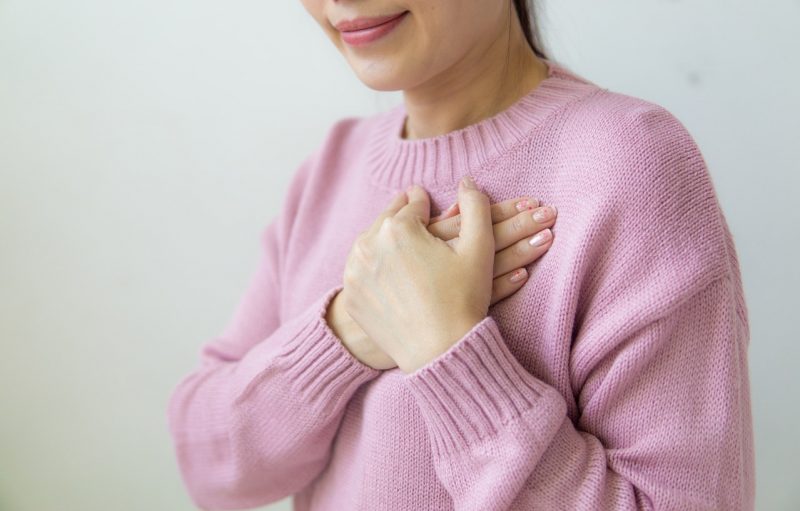 Young woman holding hands over chest.