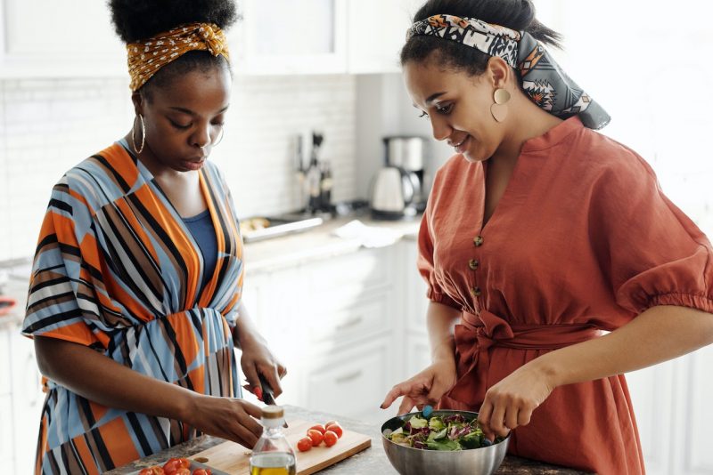 Two African American women preparing healthy food options in kitchen.