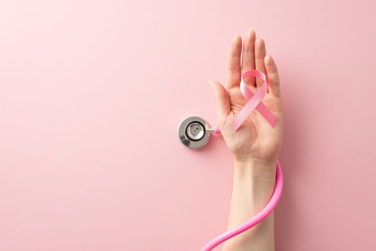 Hand holding a pink ribbon for Breast Cancer Awareness with a stethoscope, symbolizing the importance of routine checkups and proactive medical maintenance like mammograms.